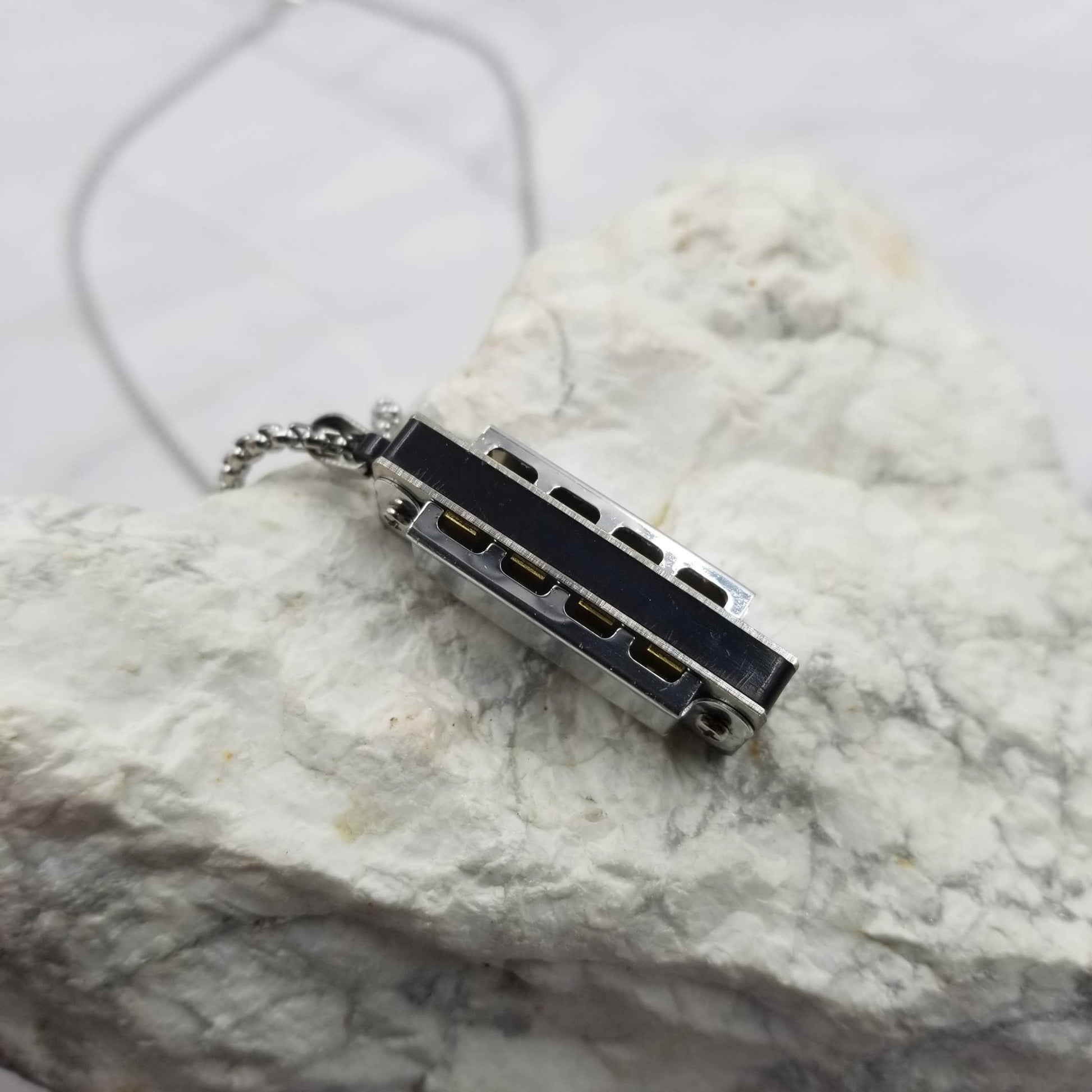 Small black and silver harmonica pendant on a marble surface