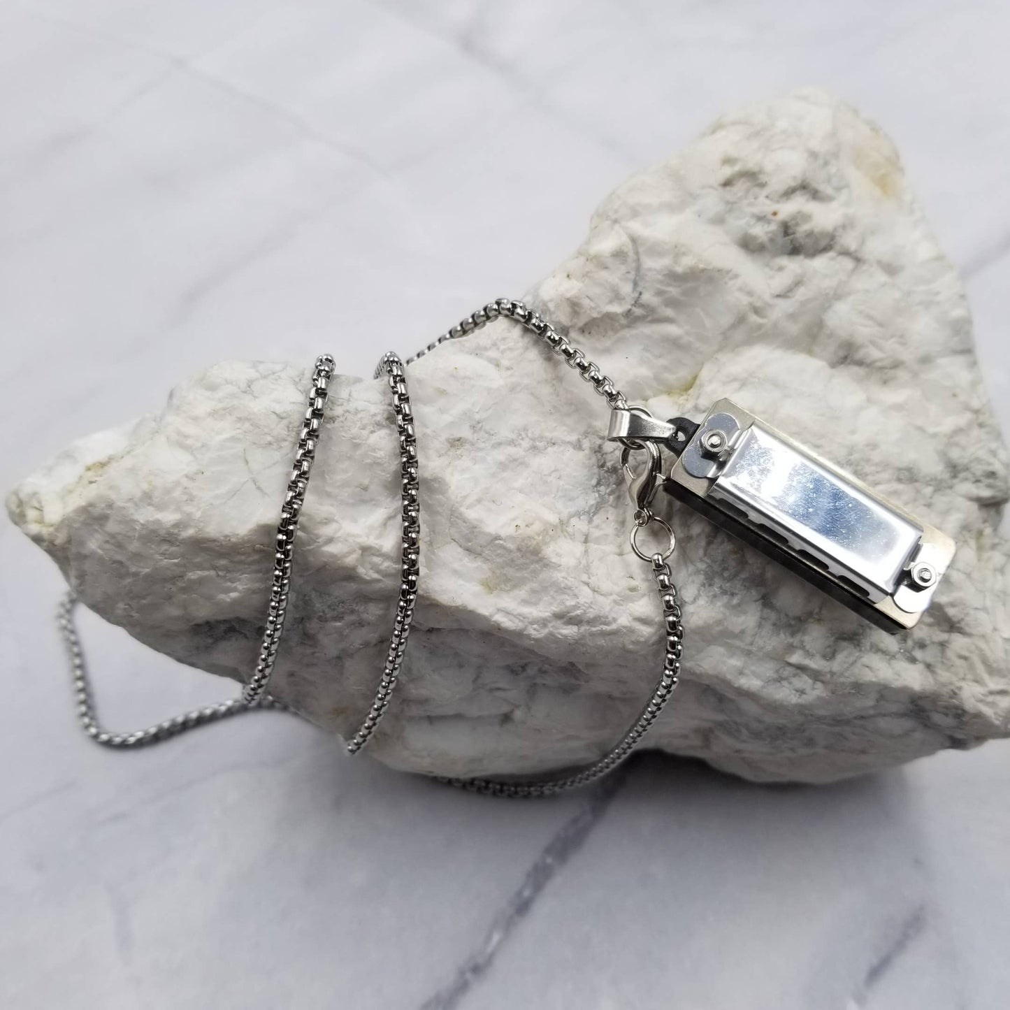 Silver harmonica necklace with a clasp on a textured white surface