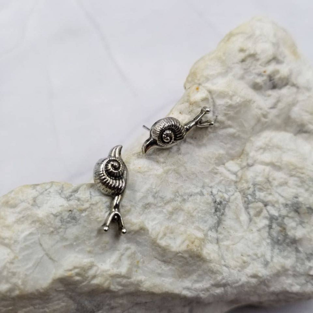 Pair of silver snail-shaped earrings on a textured stone surface