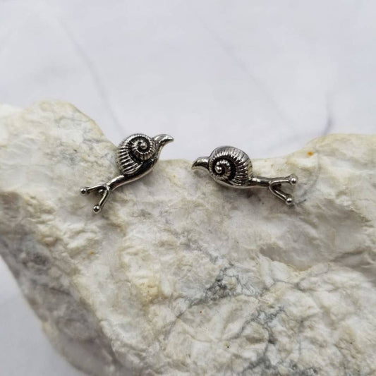 Pair of silver snail-shaped earrings on a stone surface