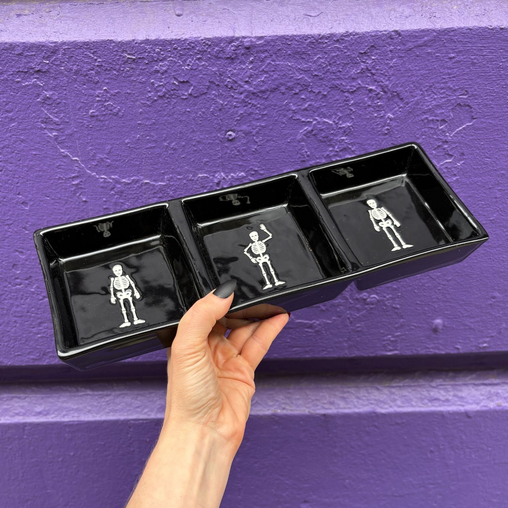 Black tray with skeleton illustrations held against a purple wall