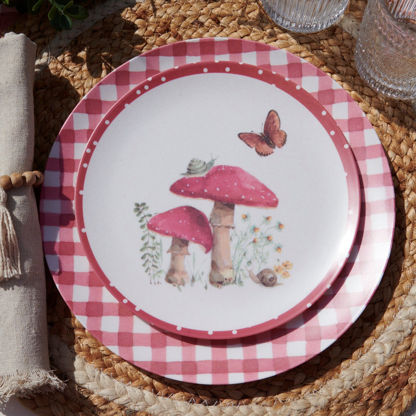 Decorative plate with pink checkered rim, mushrooms, and a butterfly on a woven surface.