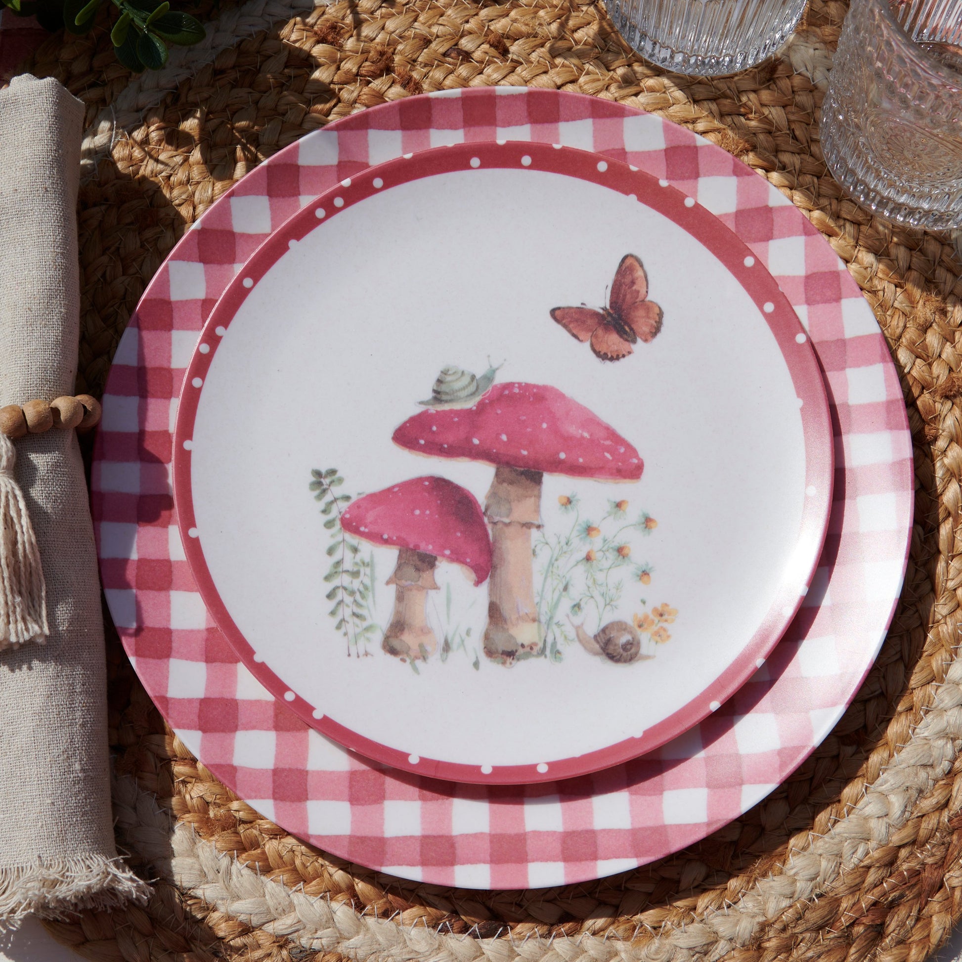 Decorative plate with pink checkered rim, mushrooms, and a butterfly on a woven surface.