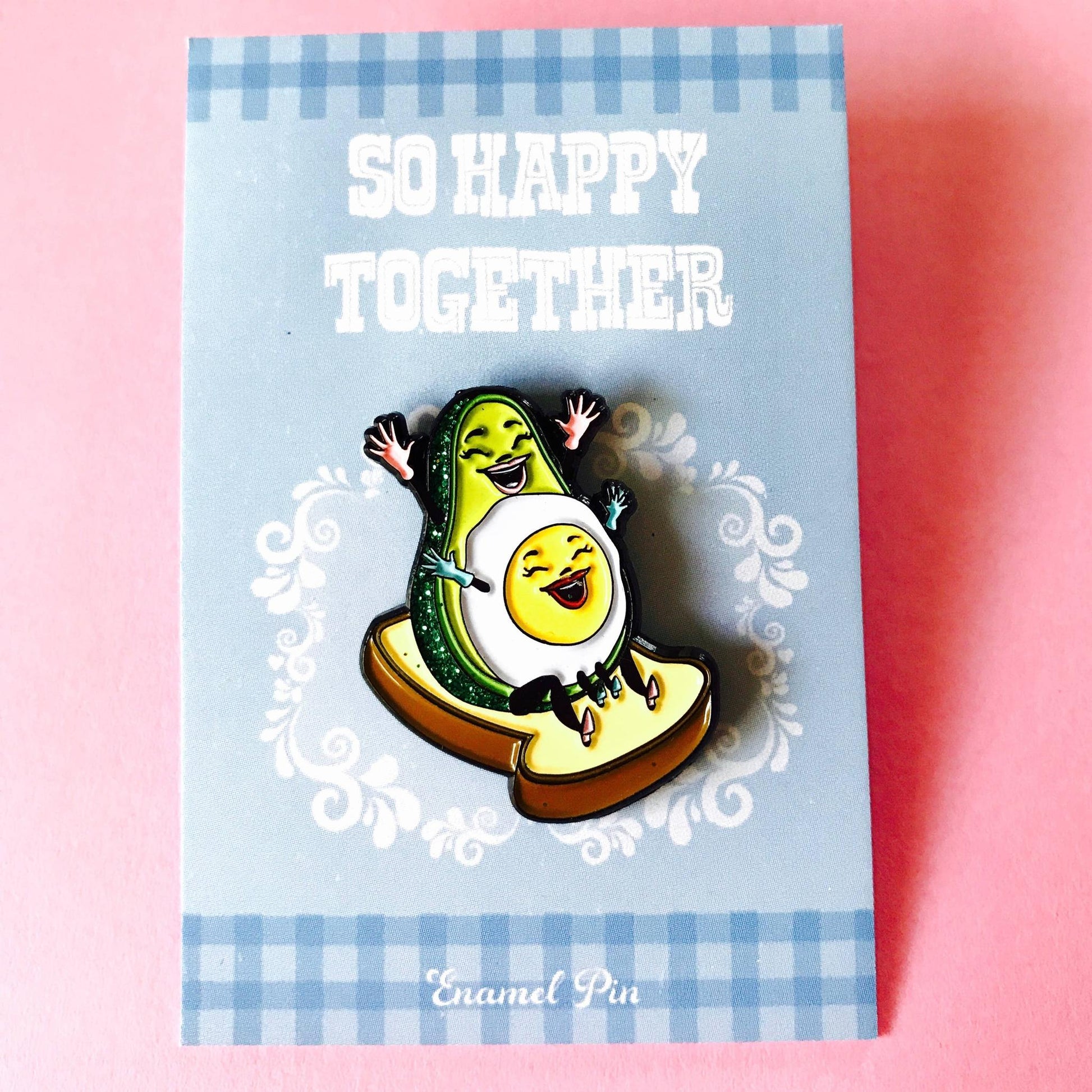 Enamel pin with avocado and egg design on a blue card with 'So Happy Together' text.