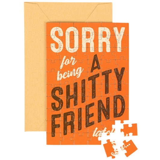 Greeting card with 'Sorry for being a shitty friend' text and puzzle pieces on an orange background.