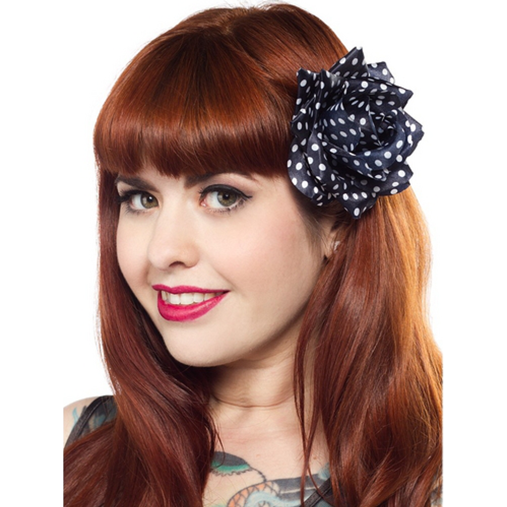 Woman with red hair wearing a navy blue flower with white polka dots in her hair on a white background