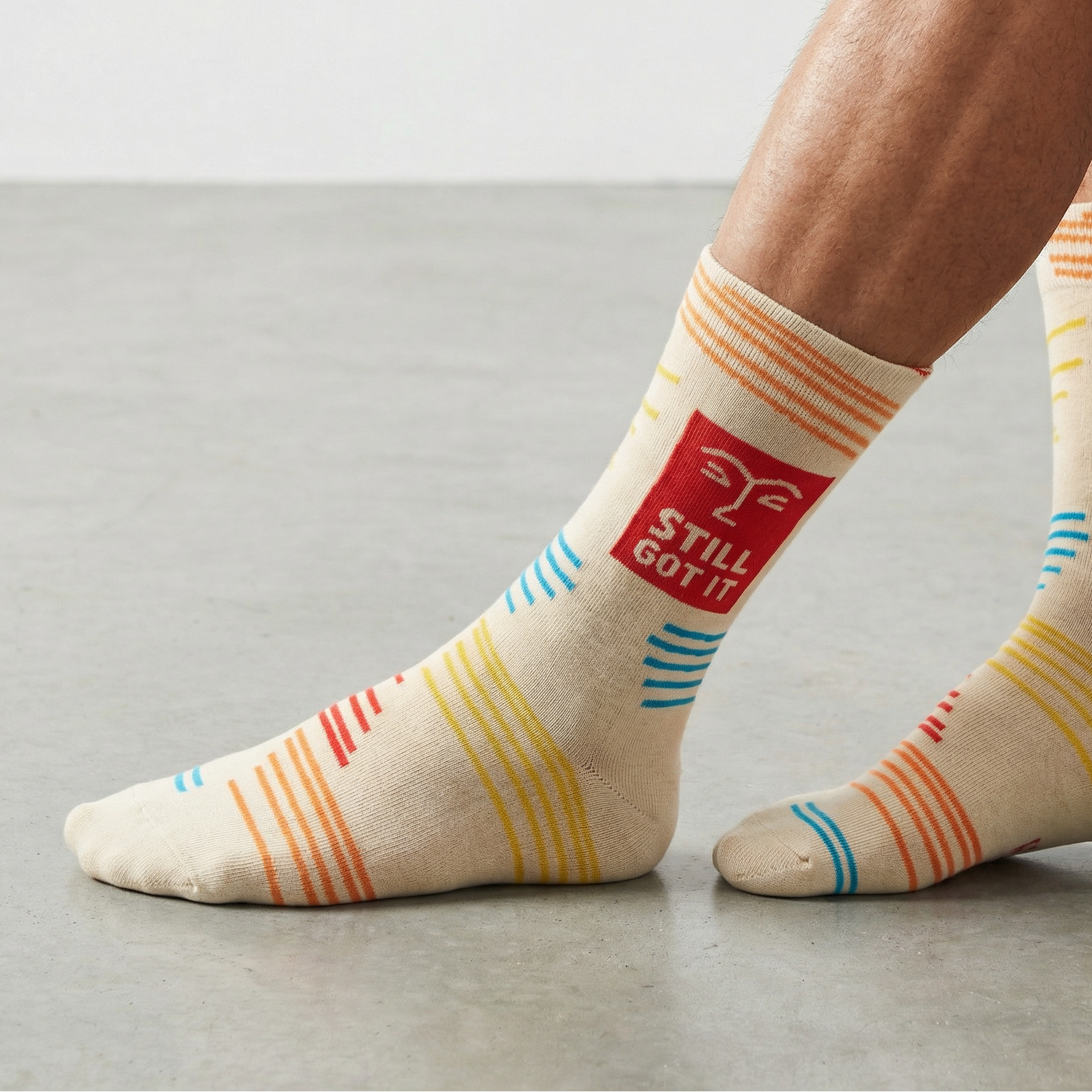 Beige socks with colorful stripes and 'Still Got It' text worn by a person on a neutral background