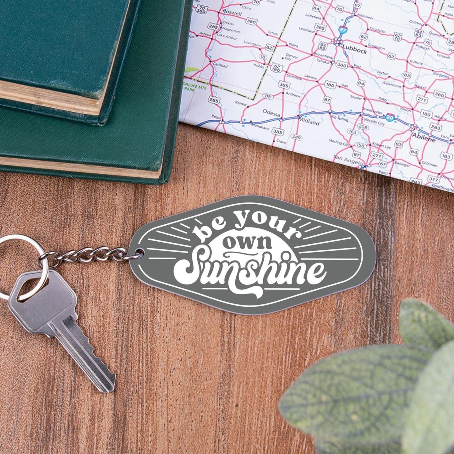 Keychain with 'be your own sunshine' tag on a wooden surface with a map and book.