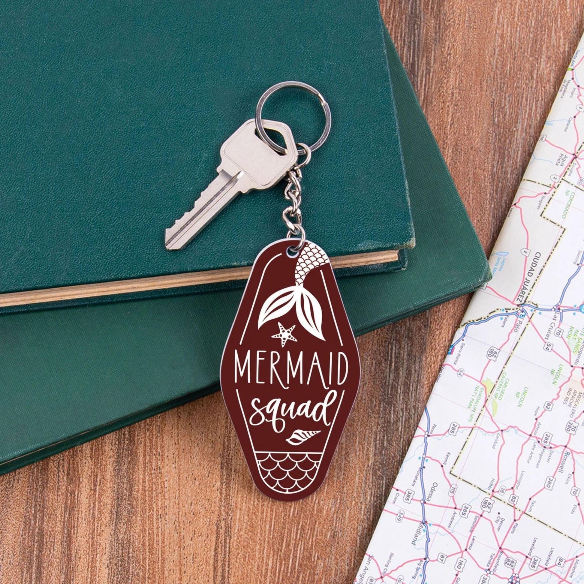 Keychain with 'Mermaid Squad' design on a wooden surface with a key and map.