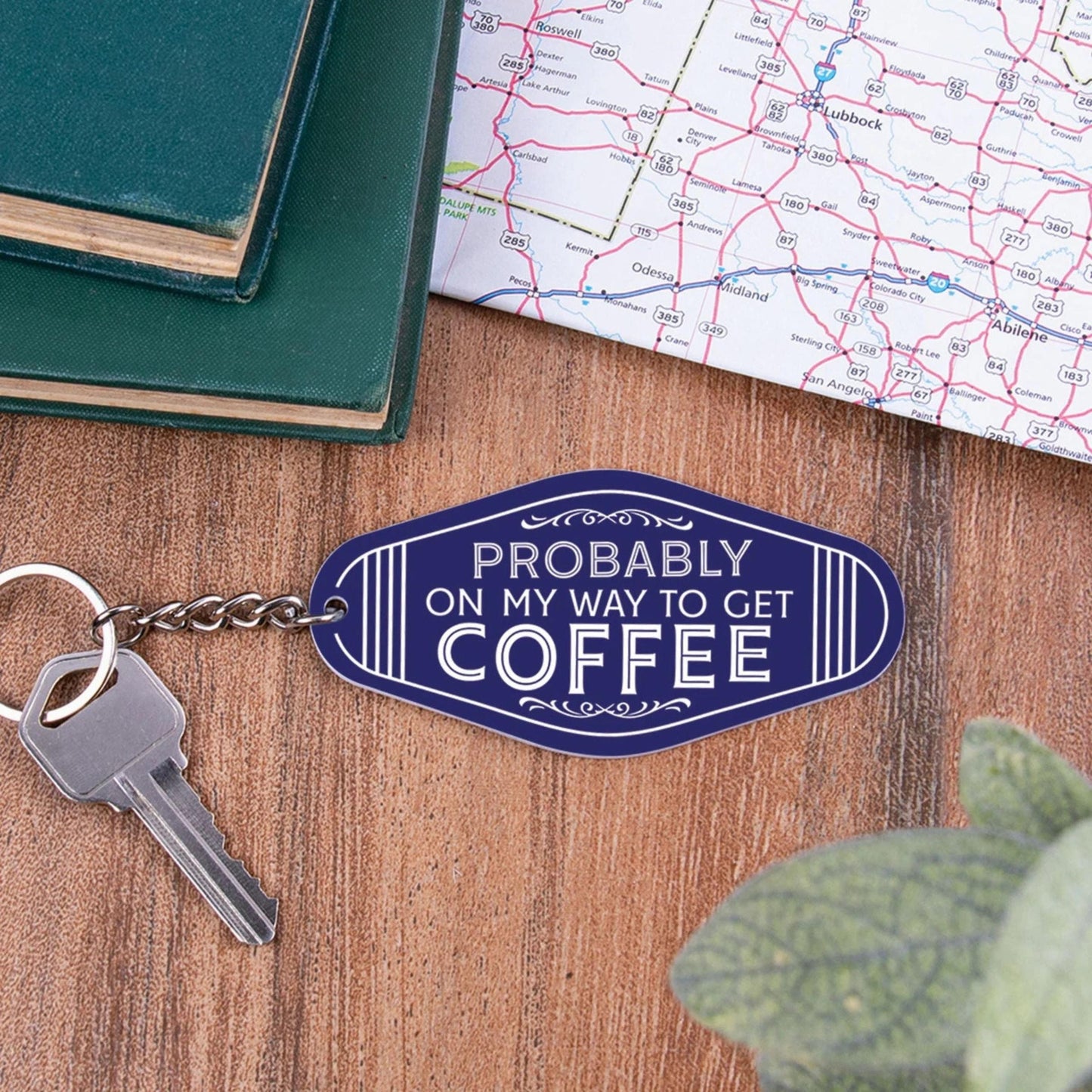 Keychain with 'Probably on my way to get coffee' tag on a wooden surface with a map and book.