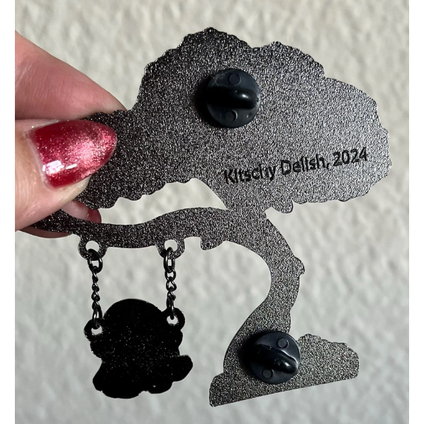 Back part of an enamel pin with 'Kitschy Delish, 2024' text on a textured white background.