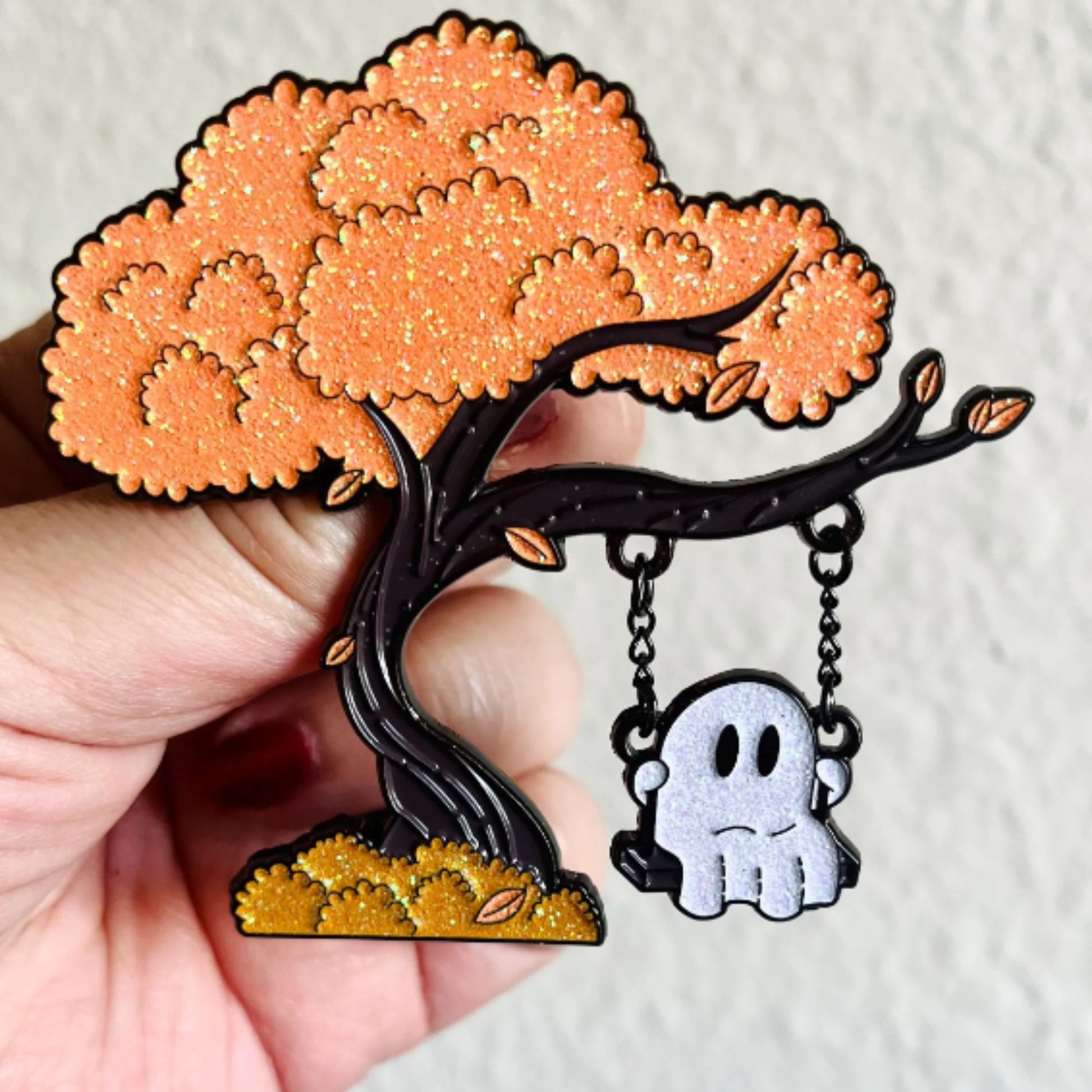 Tree-shaped brooch with a ghost character hanging from a swing on a white background