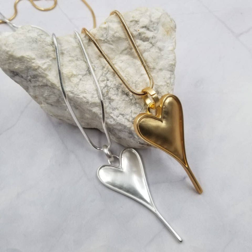 Two heart-shaped pendants, one gold and one silver, on a textured surface.