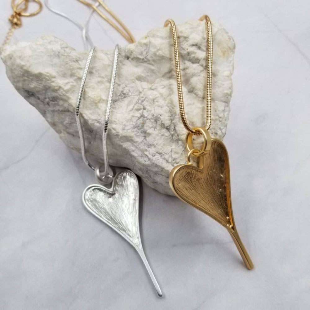 Two heart-shaped pendants, one silver and one gold, on a rock with a light gray background.