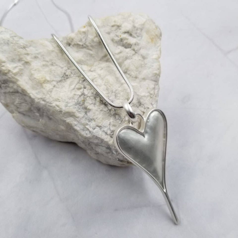 Silver heart-shaped pendant on a chain against a marble background