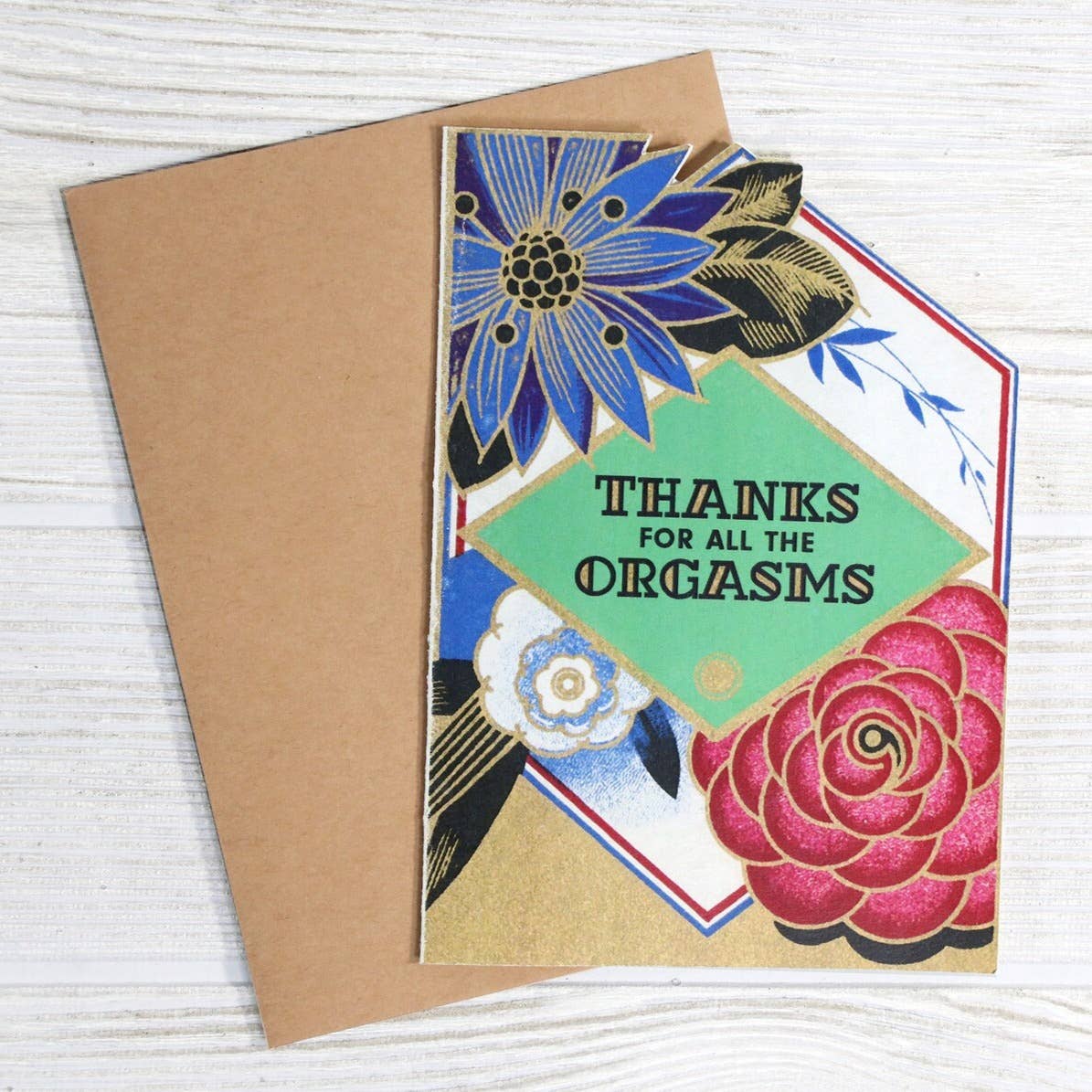 Greeting card with floral design and text 'Thanks for all the orgasms' on a wooden surface.