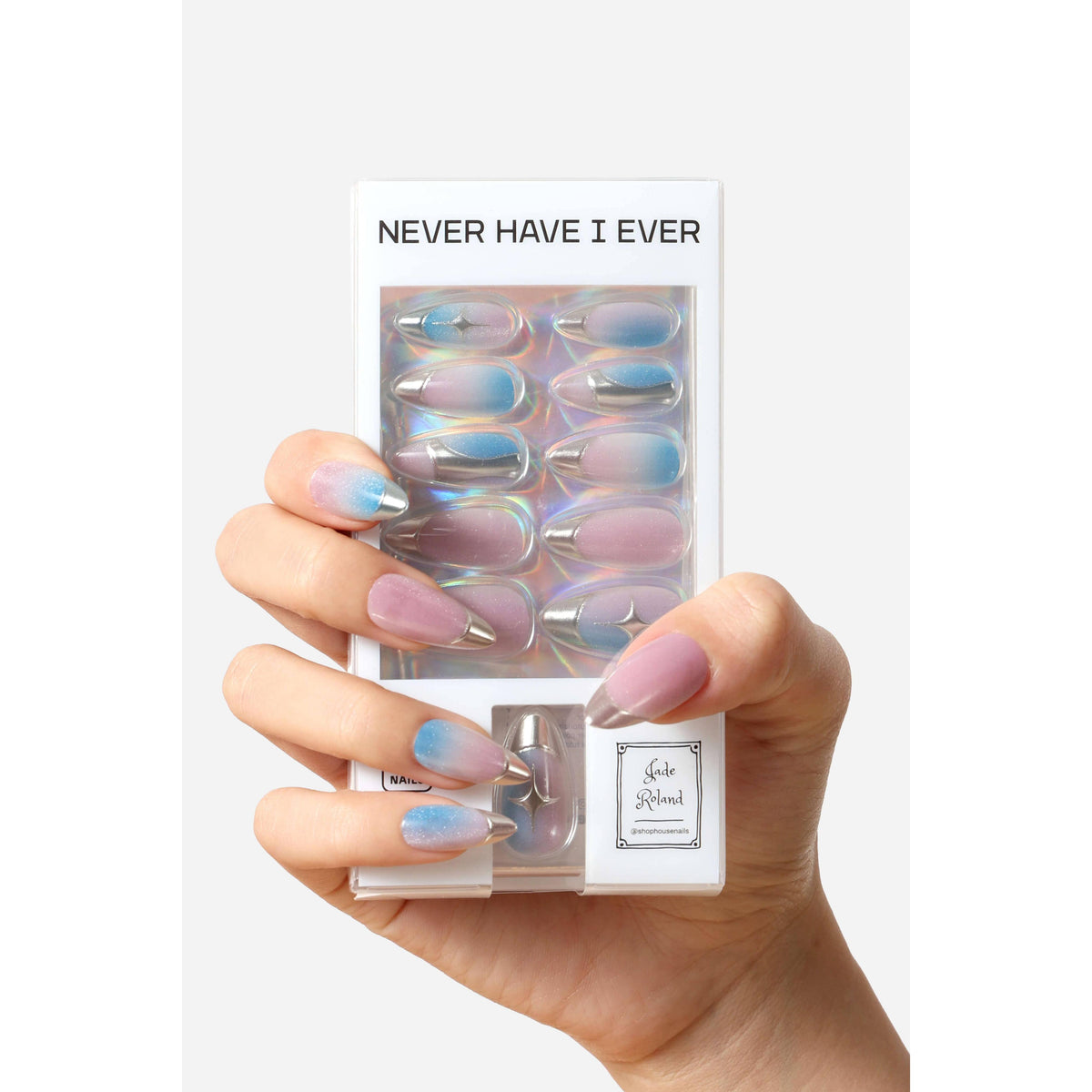 A hand holding a package of false press-on nails. The nails have a pastel gradient design transitioning from lavender-pink to light blue, with a metallic silver glitter accent at the tips.