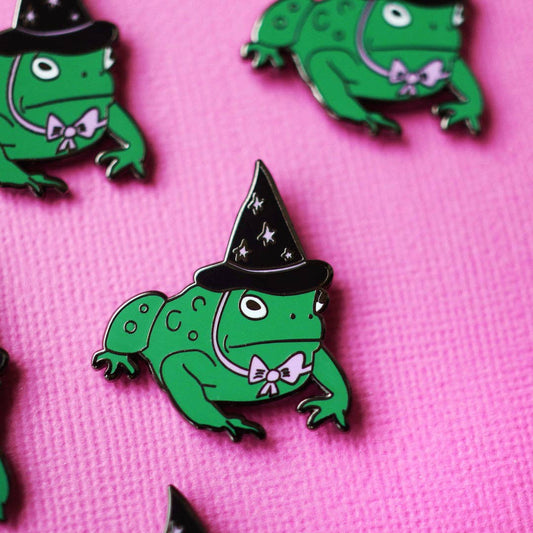 Green frog pins with witch hats on a pink background