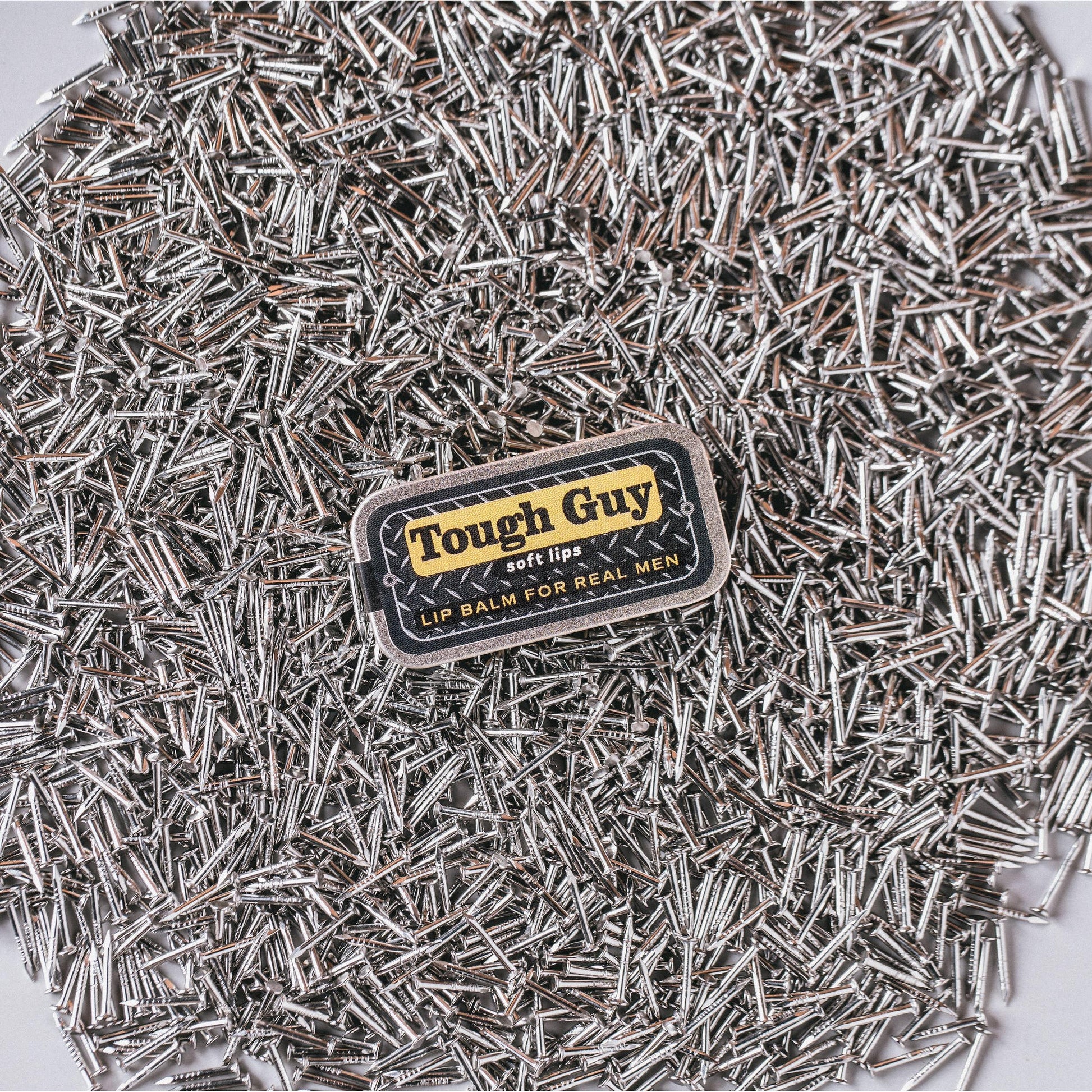 Tough Guy lip balm surrounded by small metal objects on a white background