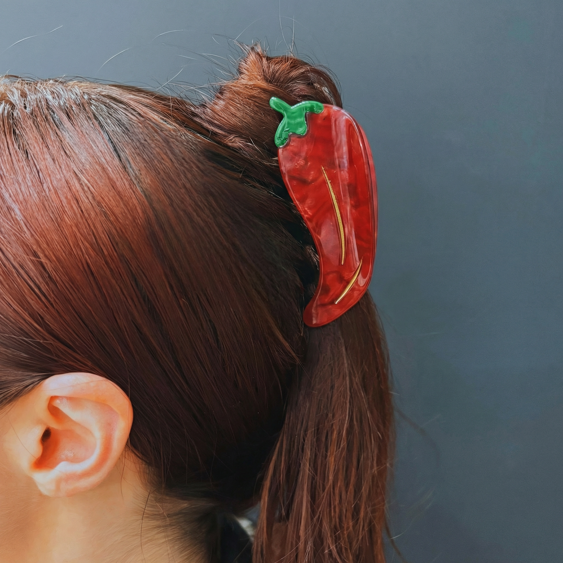 Red pepper-shaped hair clip on a person's hair against a dark background