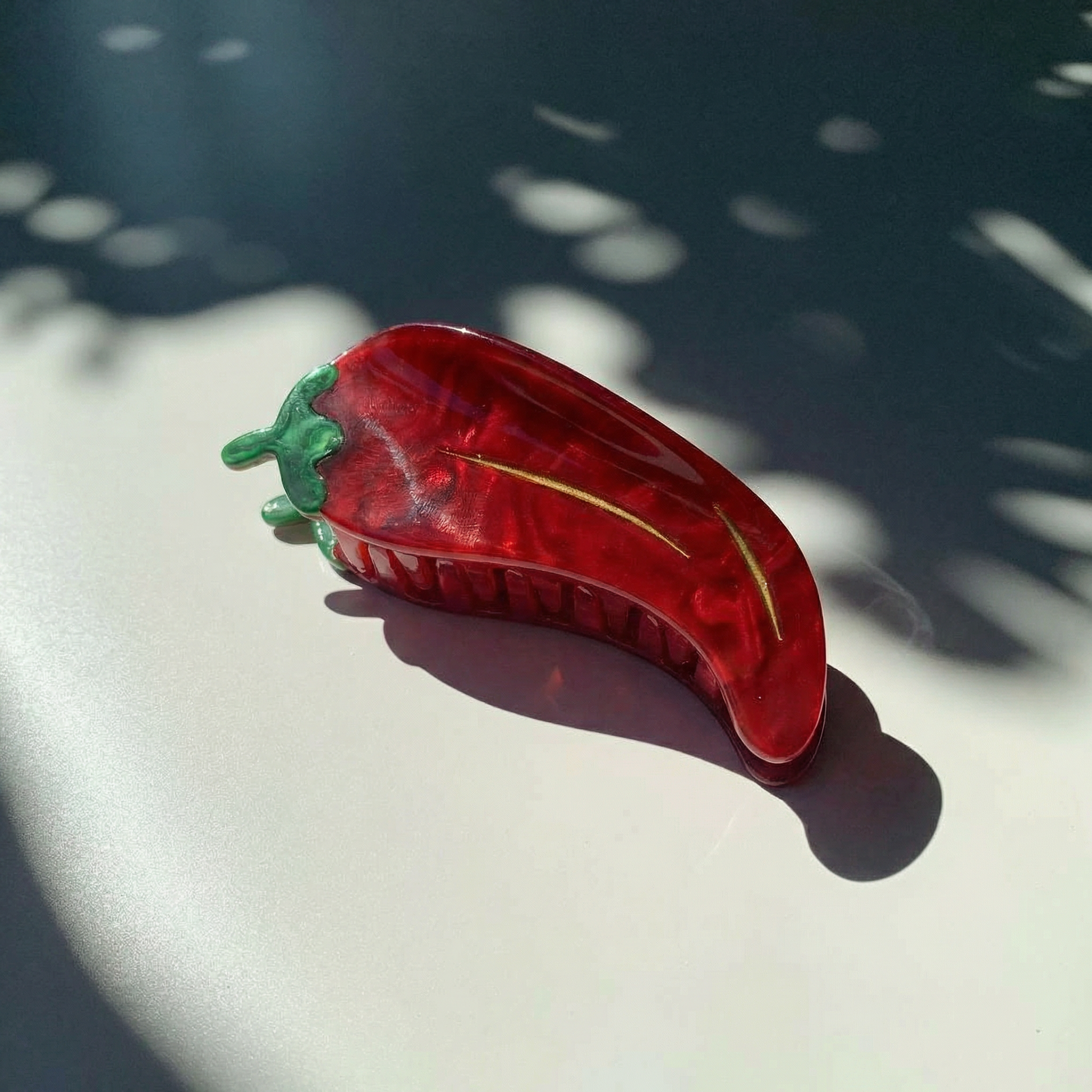 Red pepper-shaped hair clip on a white surface with shadows