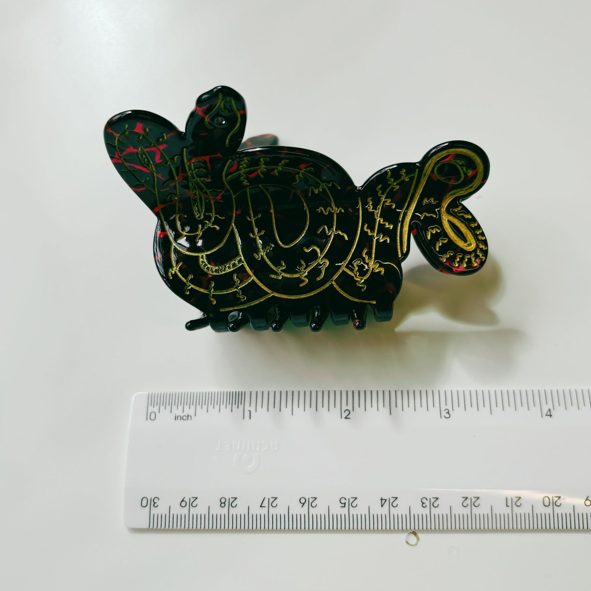 Decorative black and gold snake-shaped object next to a ruler on a white background