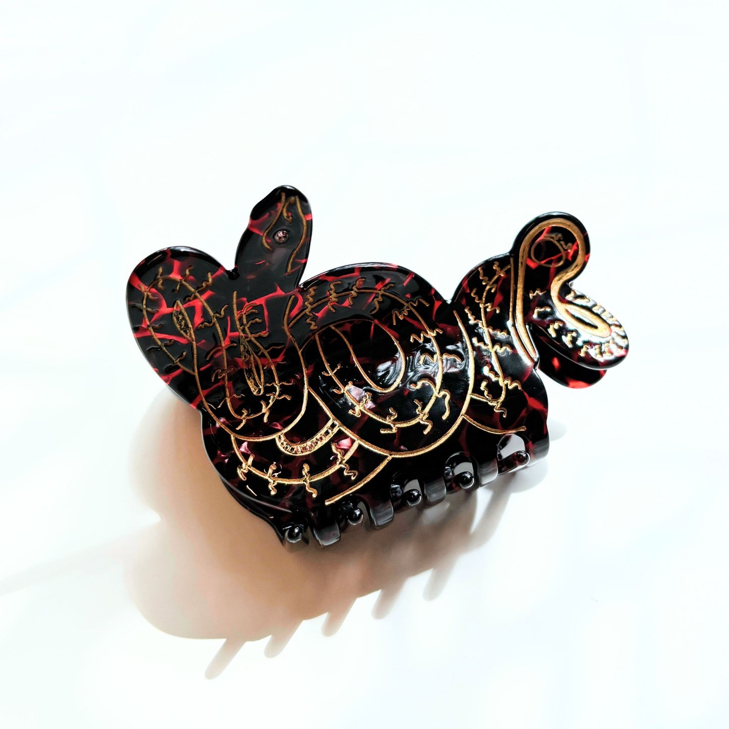 Decorative hair clip with intricate black, red, and gold design on a white background