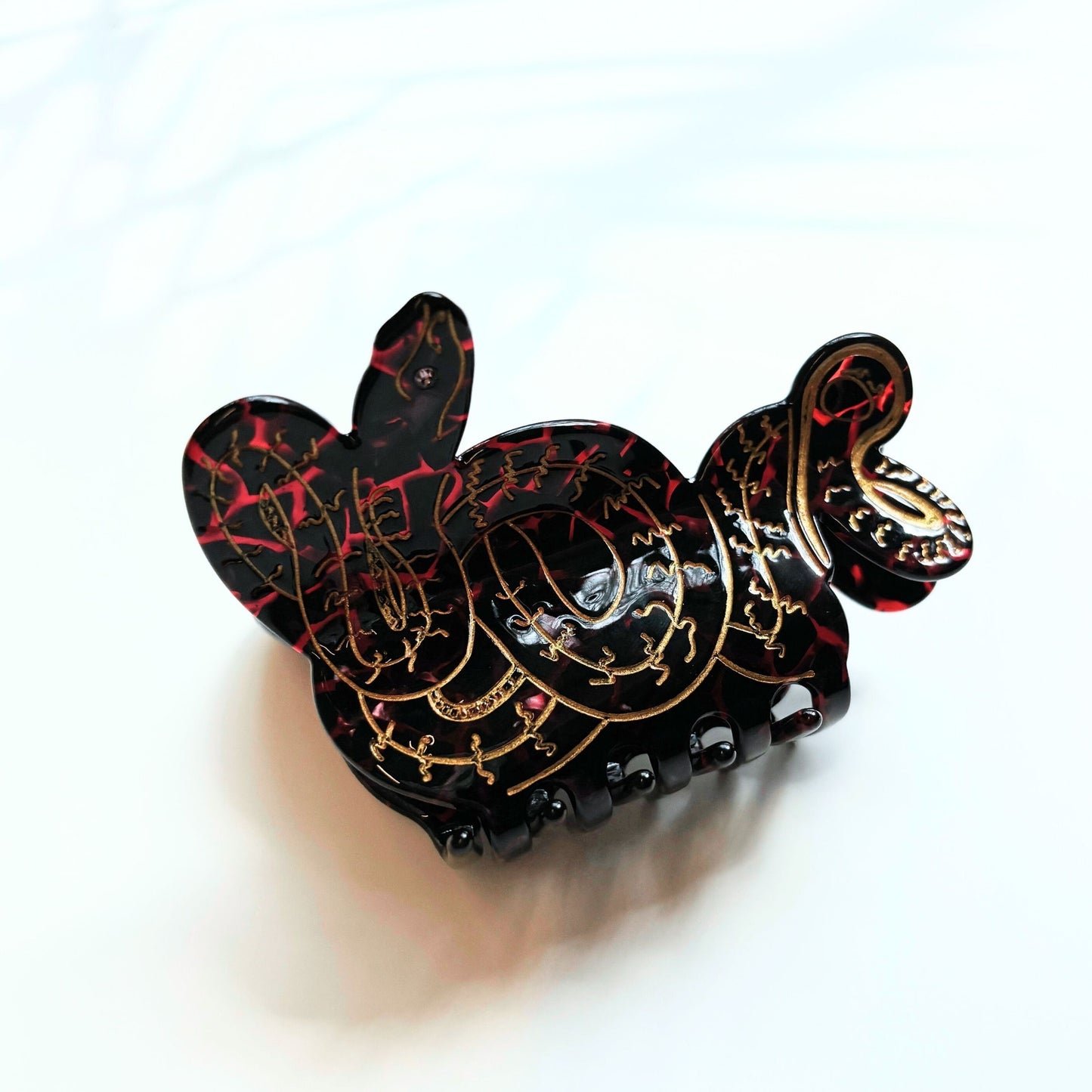 Decorative hair clip with black, gold, and red design on a white background