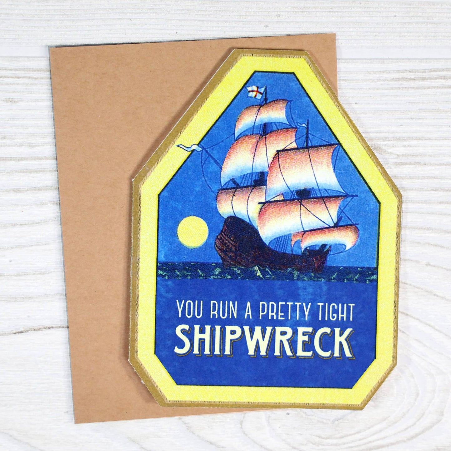 Greeting card with ship illustration and humorous text on a wooden surface