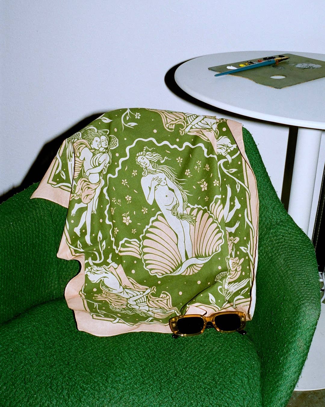 Green patterned scarf draped over a green chair with sunglasses