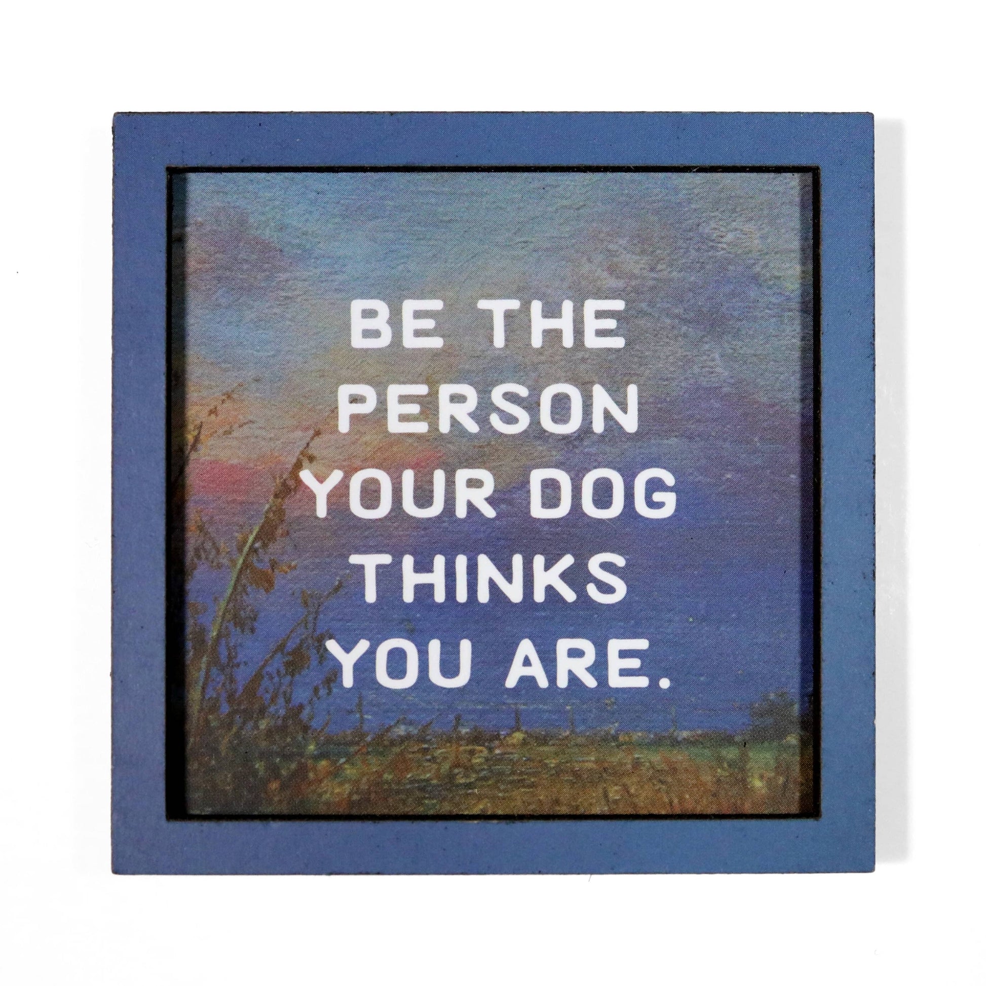 Magnet with a motivational quote 'Be the person your dog thinks you are' against a scenic background.