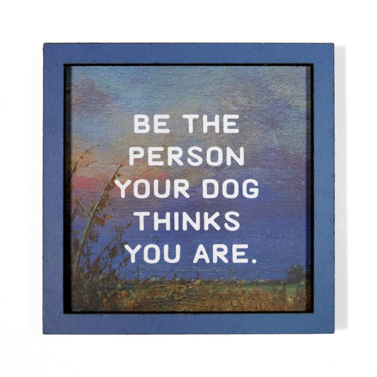 Magnet with a motivational quote 'Be the person your dog thinks you are' against a scenic background.