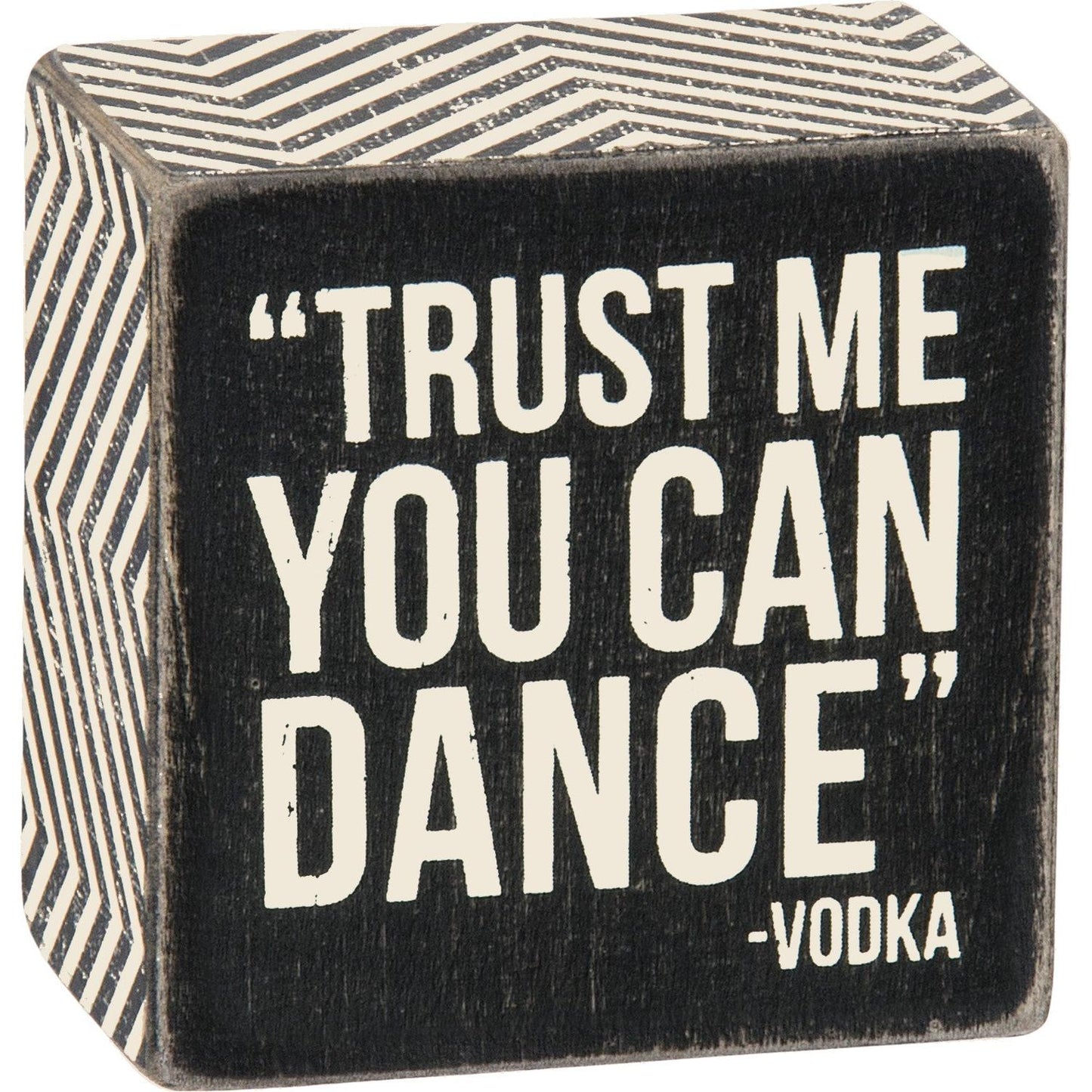 A classic black and white wooden box sign lending a distressed "'Trust Me You Can Dance' - Vodka" sentiment with zigzag patterned trim, close up shot.